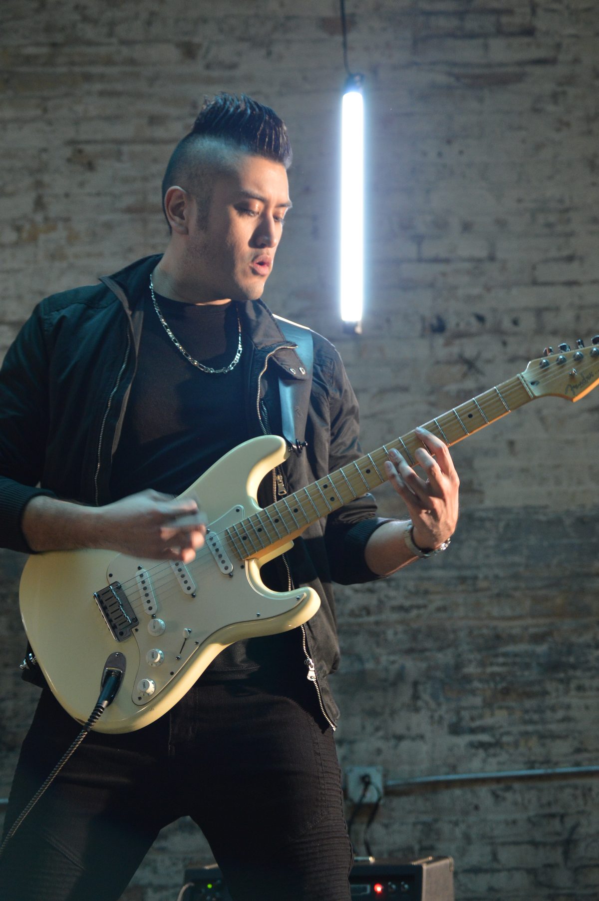 La Obra guitarist playing against a brick wall